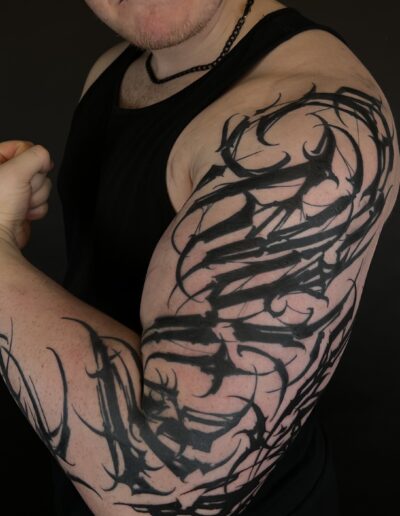 A client's arm showcasing a large, custom freehand blackwork tattoo by Goorazz, featuring dynamic abstract calligraphy and neotribal-inspired patterns, created in London at Parliament Tattoo