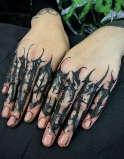 A close-up of a client's hands showcasing intricate custom freehand blackwork finger tattoos by Goorazz, blending abstract calligraphy with a dark-themed neotribal influence, created in London at Parliament Tattoo