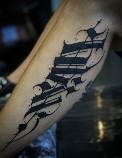 A close-up of a client's calf featuring a bold, custom freehand blackwork tattoo by Goorazz, integrating dynamic abstract calligraphy and dark-themed expressive elements, created in London at Parliament Tattoo