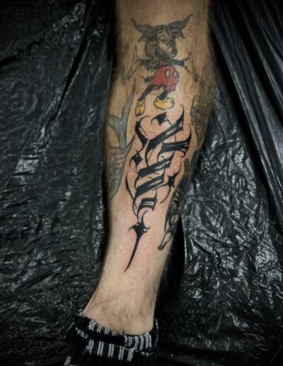 A client's calf featuring a bold, custom freehand blackwork tattoo by Goorazz, integrating dynamic abstract calligraphy and dark-themed expressive elements, created in London at Parliament